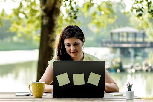 Girl remotely working near a lake with a coffee mug on the table.