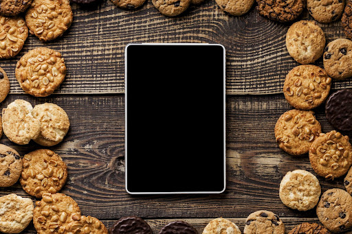 A picture of a tablet/ipad on a wooden table surrounded with actual edible cookies.